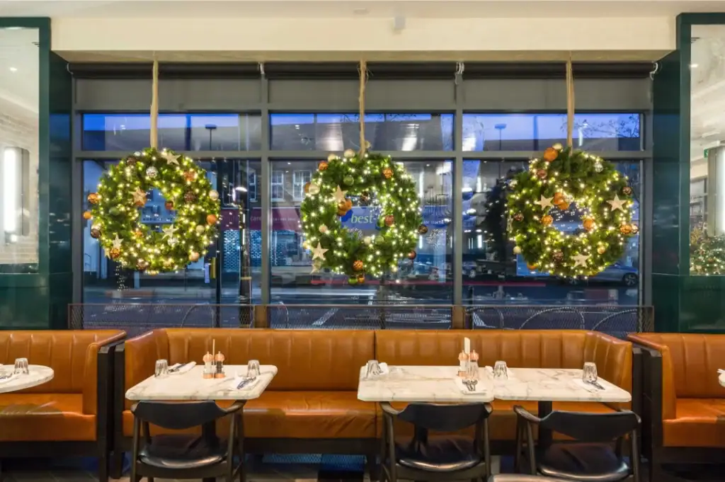 three decorated Christmas wreaths with lights fixed to windows in restaurant